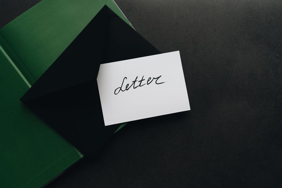 A flatlay showcasing a black envelope with a calligraphy letter, offering ample copyspace on a dark background.